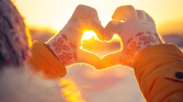 Person mit Handschuhen macht Herz mit Händen