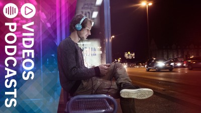 Mann sitzt mit Kopfhörern an einer Haltestelle.