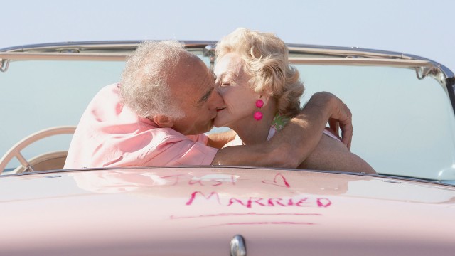 Älteres Paar in einem rosa Cabrio küsst sich