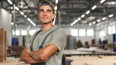 Junger Mann steht in einer Produktionshalle in Arbeitsuniform