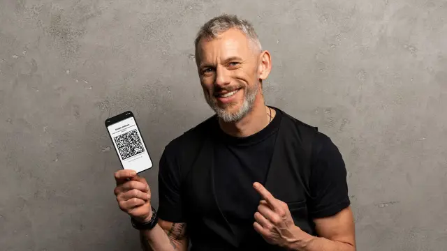 Mann hält ein handy hoch, zeigt mit seinem Finger darauf und lächelt.