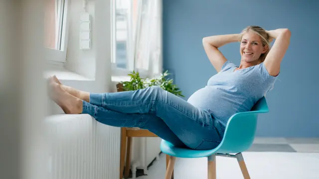 Schwangere Frau lehnt sich entspannt zurück.