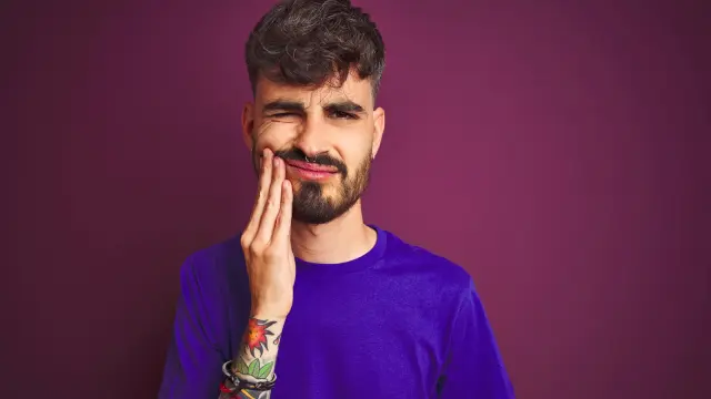 Junger Mann fasst sich an seine Backe und verzieht schmerzhaft das Gesicht.