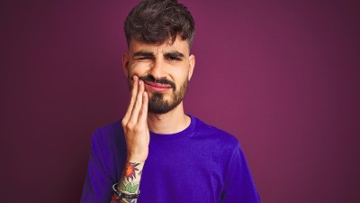 Mann fasst sich an Backe und verzieht sein Gesicht