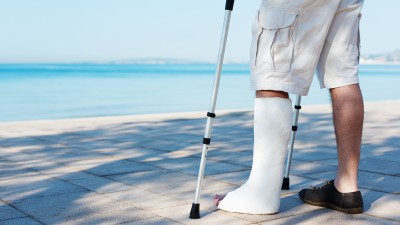 Ein Mann steht mit Gipsbein und Krücken am Meer