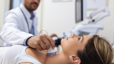 Ein Arzt untersucht mit einem Ultraschallgerät die Schilddrüse einer Frau.