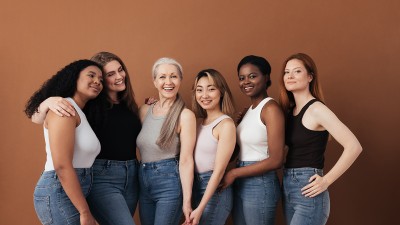 Frauen unterschiedlichen Alters posieren gemeinsam vor braunem Hintergrund