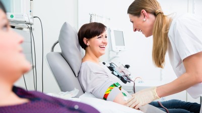 Eine Krankenschwester beugt sich über eine Patientin, um ihr Blut abzunehmen.