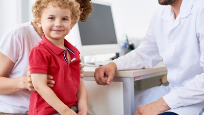Ein kleiner Junge sitzt auf dem Schoß seiner Mutter im Behandlungszimmer einer Arztpraxis.
