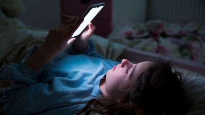 Ein Mädchen liegt im Dunkeln in ihrem Bett und starrt auf das Handy.