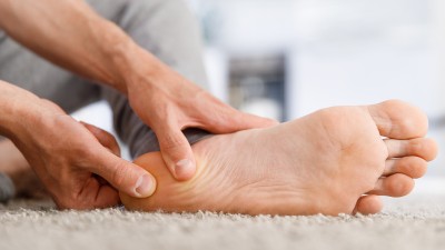 Die Hände eines Mannes geben dem eigenen Fuß eine Massage an der Ferse