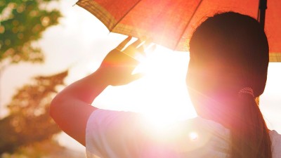 Eine junge Frau ist von hinten zu sehen. Sie hält einen Sonnenschirm und die Hand in die Höhe, um das Sonnenlicht abzuschirmen.