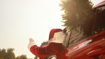 Weihnachtsmann in rotem Auto mit Weihnachtsbaum, der aus dem Fenster winkt.