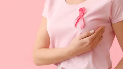 Eine Frau mit pinker Schleife auf dem Shirt tastet ihre Brust ab.