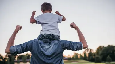 Ein Vater trägt seinen Sohn auf den Schultern.