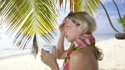 Eine Frau steht mit Schal und einer Tasse Tee am Strand.