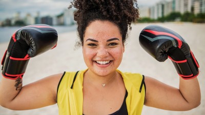 Eine Frau trägt Boxhandschuhe und demonstriert ihre Stärke, indem sie die Hände lächelnd nach oben hält.