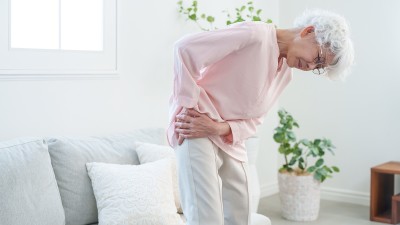 Eine ältere Frau fasst sich vor Schmerzen an die Hüfte.