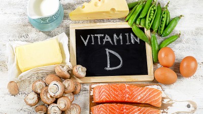 Um eine Tafel, auf der „Vitamin D“ steht, sind verschiedene Lebensmittel arrangiert.