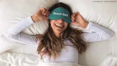 Frau mit Bosch BKK Schlafmaske liegt lachend im Bett
