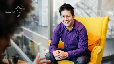 Ein Mann sitzt auf einem gelben Sessel gegenüber einer anderen Person.