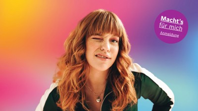 Junge Frau, augenzwinkernd, vor buntem Hintergrund in Regenbogenfarben