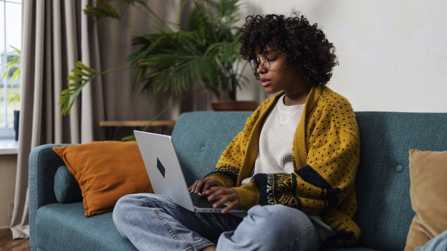 Junge schwarze Frau, mit Laptop auf dem Sofa sitzend