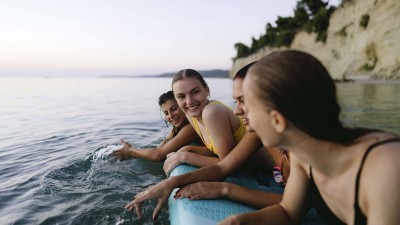 4 junge Frauen, die sich an einem SUP-Board festhalten und im Wasser treiben